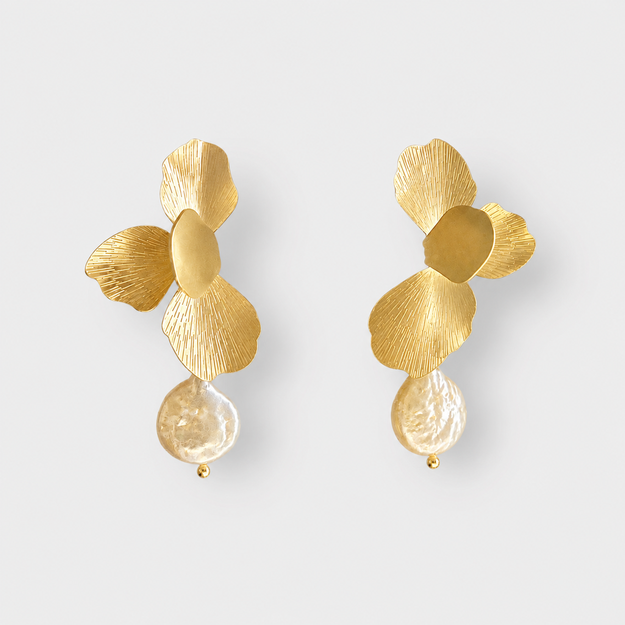 A pair of gold flower-shaped drop earrings with textured petals and a clear teardrop-shaped bead hanging below, shown on a light gray background.